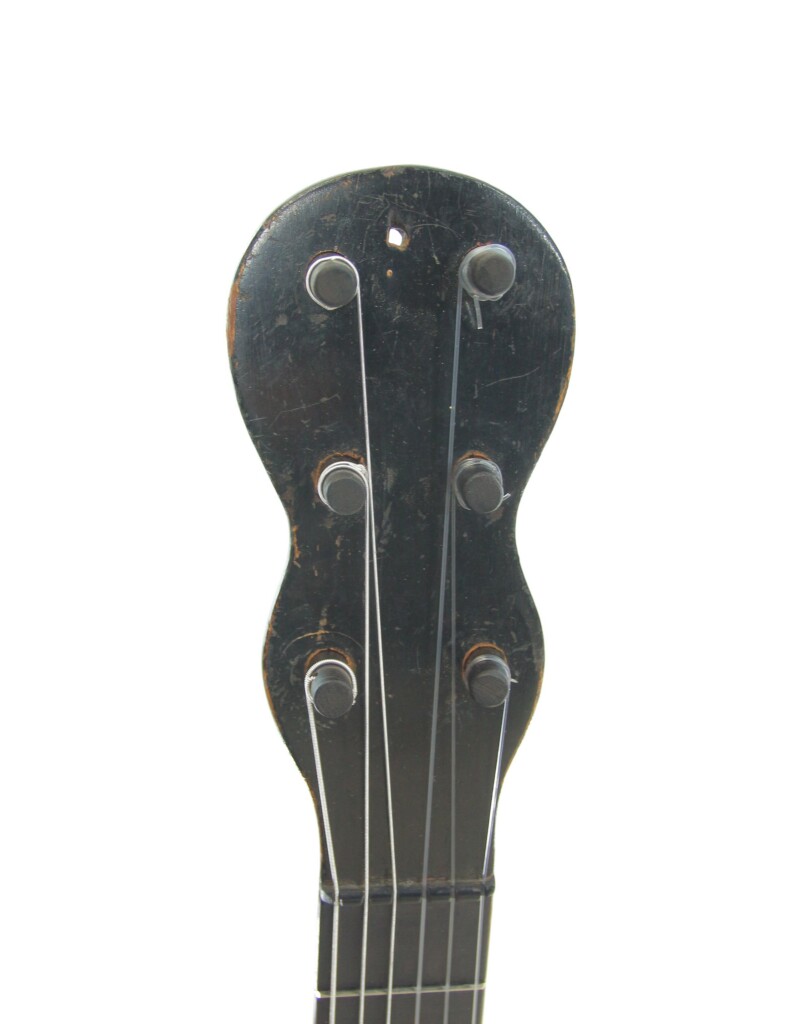 Nahaufnahme Der Schwarzen Kopfplatte Der Französischen Romantikgitarre Aus Den 1860Er Jahren Mit Vier Stimmwirbeln Und Metallsaiten, Vor Einem Schlichten Weißen Hintergrund.