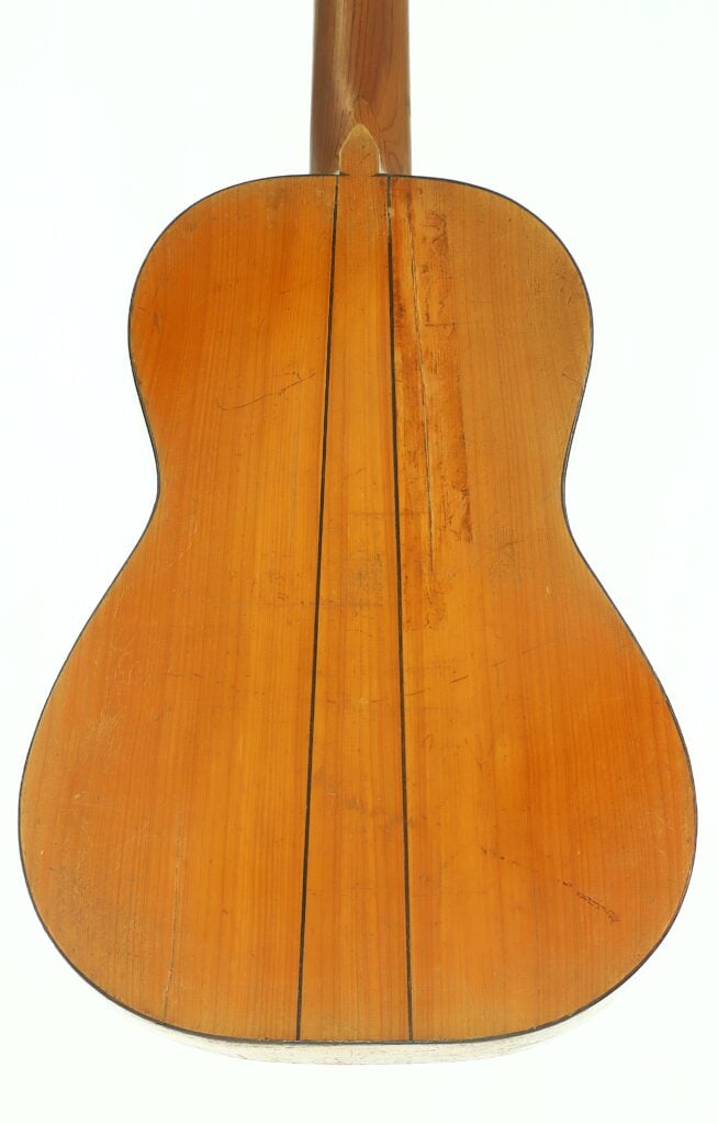 Rückansicht einer Akustikgitarre von José Ortega aus der Zeit um 1890, mit einem Holzkorpus mit sichtbarer Maserung, zwei dunklen vertikalen Linien und einer hellbraunen Lackierung, fotografiert vor weißem Hintergrund. Rückansicht einer Akustikgitarre von José Ortega aus der Zeit um 1890, mit einem Holzkorpus mit sichtbarer Maserung, zwei dunklen vertikalen Linien und einer hellbraunen Lackierung, fotografiert vor weißem Hintergrund.