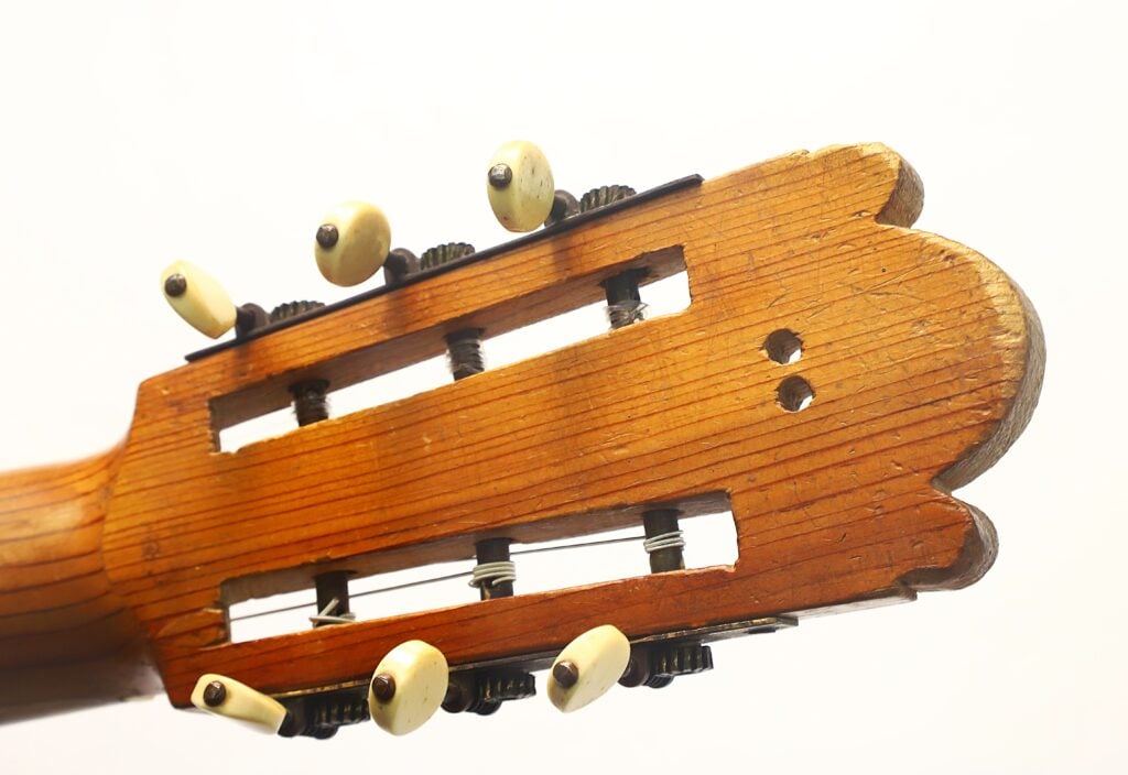Nahaufnahme des Kopfes einer klassischen Gitarre von José Ortega (ca. 1890), wobei die Stimmwirbel, die Saiten und die feine Holzmaserung vor einem schlichten weißen Hintergrund besonders hervorgehoben werden. Nahaufnahme des Kopfes einer klassischen Gitarre von José Ortega (ca. 1890), wobei die Stimmwirbel, die Saiten und die feine Holzmaserung vor einem schlichten weißen Hintergrund besonders hervorgehoben werden.