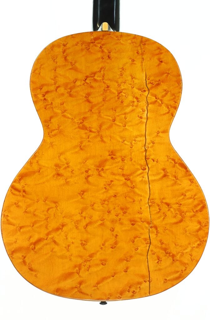 Die Rückseite der A. Klein-Akustikgitarre aus der Zeit um 1920 ist aus gemasertem Holz gefertigt und weist eine wirbelnde, gesteppte Maserung sowie einen auffälligen dunklen Riss auf, der vertikal verläuft. Die Rückseite der A. Klein-Akustikgitarre aus der Zeit um 1920 ist aus gemasertem Holz gefertigt und weist eine wirbelnde, gesteppte Maserung sowie einen auffälligen dunklen Riss auf, der vertikal verläuft.