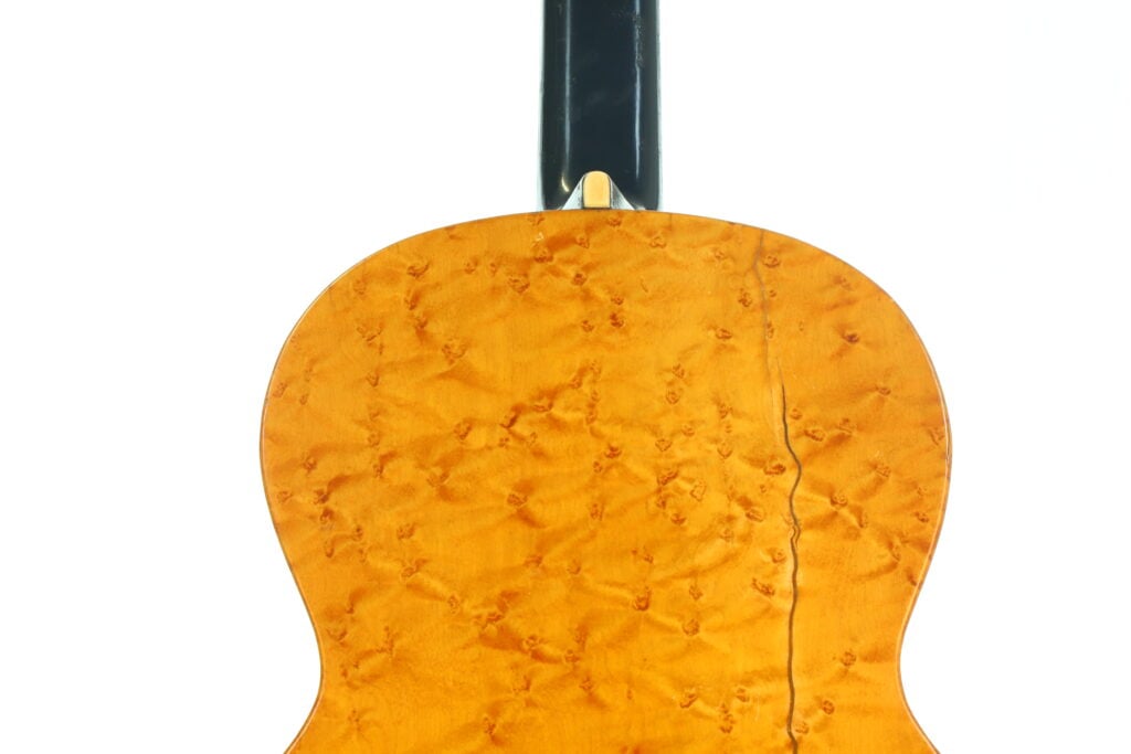 Die Rückseite der hölzernen Akustikgitarre von A. Klein aus der Zeit um 1920 weist eine helle, glänzende Lackierung und eine markante, wellenförmige Maserung auf, aus der ein schwarzer Hals herausragt. Die Rückseite der hölzernen Akustikgitarre von A. Klein aus der Zeit um 1920 weist eine helle, glänzende Lackierung und eine markante, wellenförmige Maserung auf, aus der ein schwarzer Hals herausragt.