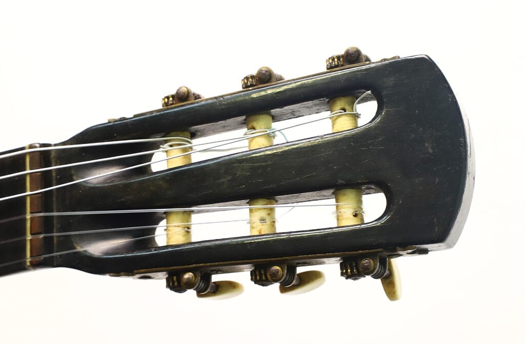 Nahaufnahme des Kopfstücks einer klassischen Gitarre von A. Klein aus der Zeit um 1920, auf der die Stimmwirbel, die Saiten und die dunkle Holzoberfläche vor weißem Hintergrund zu sehen sind. Nahaufnahme des Kopfstücks einer klassischen Gitarre von A. Klein aus der Zeit um 1920, auf der die Stimmwirbel, die Saiten und die dunkle Holzoberfläche vor weißem Hintergrund zu sehen sind.