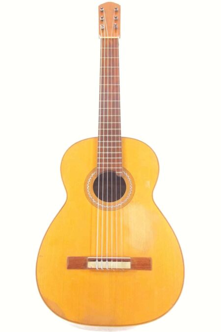 The Casa Gonzalez 1910 Classical Guitar, with a light wooden body, six strings, and a round rosette-adorned sound hole, is shown upright against a white background.