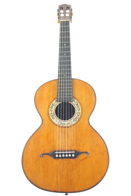 The Markneukirchen ~1870 is a vintage acoustic guitar featuring a wooden body, six strings, decorated sound hole, and dark tuning pegs, shown against a white background.