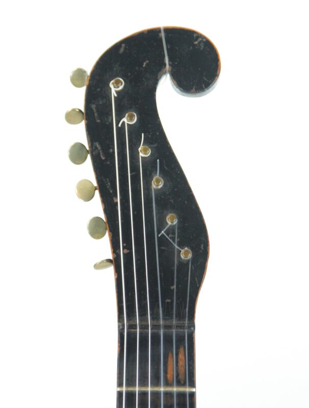 Close-up of the Stauffer Style ~1830 Romantic Guitars black scroll-shaped headstock with six left-side tuning pegs and visible strings, set against a white background.