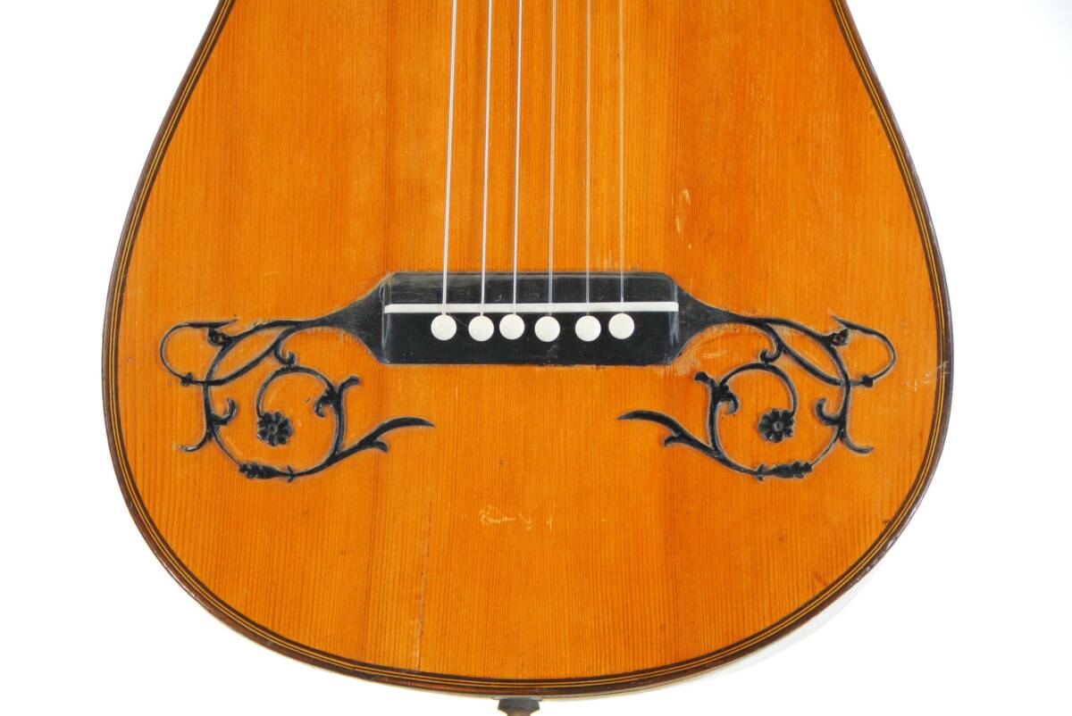Close-Up Of The Karl Frey Baroque Guitar Body, Showing Its Six Strings, Black Bridge With White Pegs, And Intricate Black Floral Designs On Both Sides.