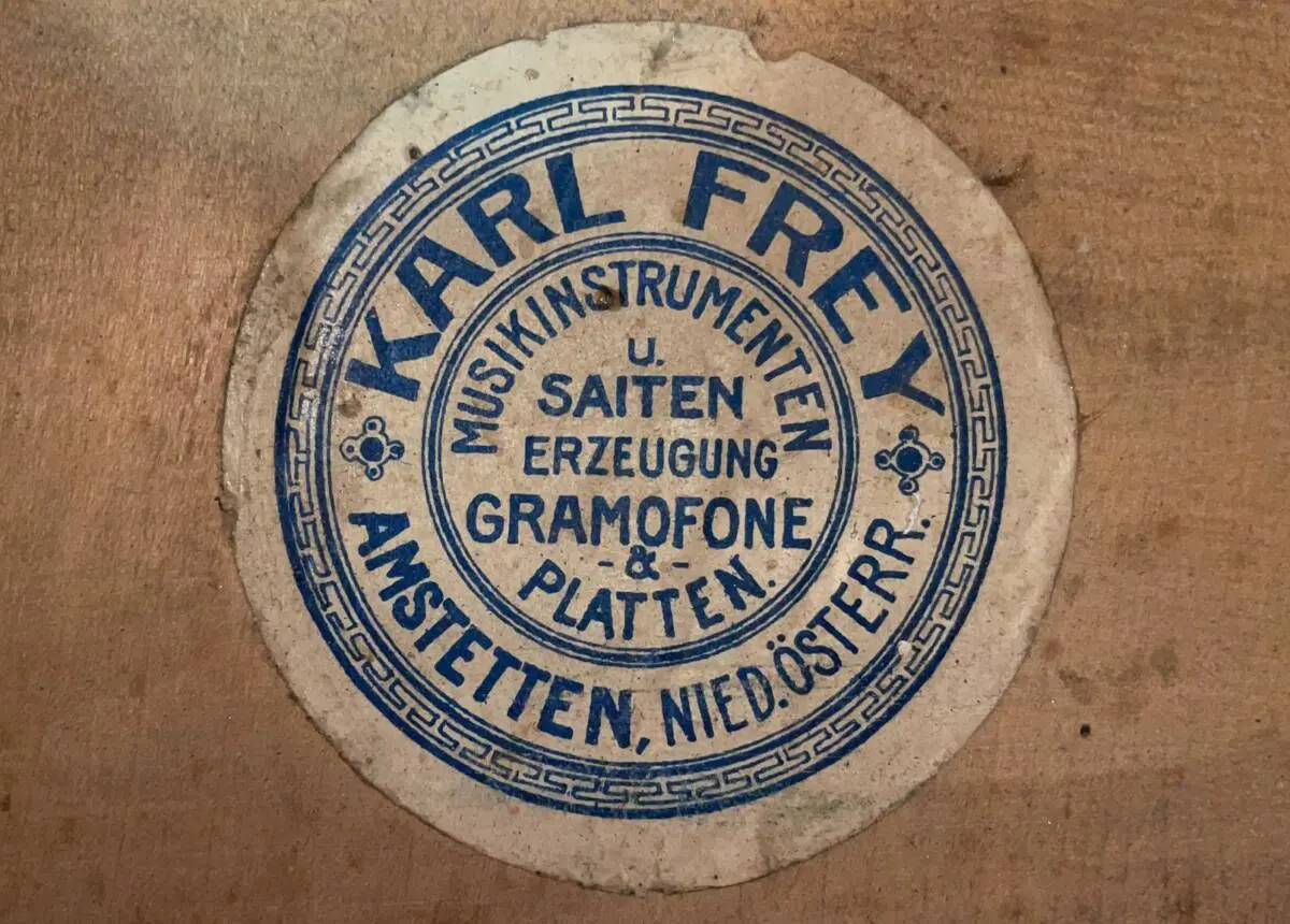 A Circular Vintage Label With Blue Text Reading “Karl Frey Musikinstrumenten U. Saiten Erzeugung Gramofone &Amp; Platten. Amstetten, Nied. Österr.” On Beige, Reflecting The Karl Frey Baroque Guitar’s Legacy And Craftsmanship.