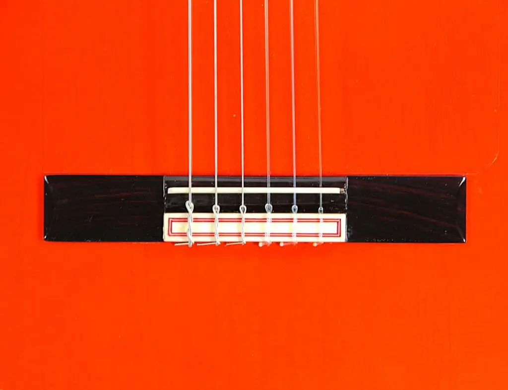 Nahaufnahme Der Hermanos Conde 1999 Paco De Lucia Spezial-Flamenco-Gitarre Mit Schwerpunkt Auf Dem Schwarzen Steg, Dem Weißen Sattel, Den Sechs Saiten Und Dem Leuchtend Orangefarbenen Korpus.