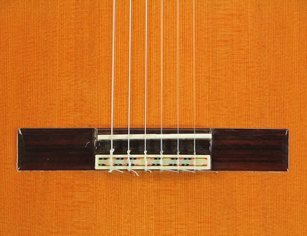 Nahaufnahme Des Stegs Und Der Sechs Saiten Einer Manuel Rodriguez Jr Klassischen Gitarre, Die Ihren Holzkorpus Mit Strukturiertem Orange-Braunem Finish Hervorhebt.