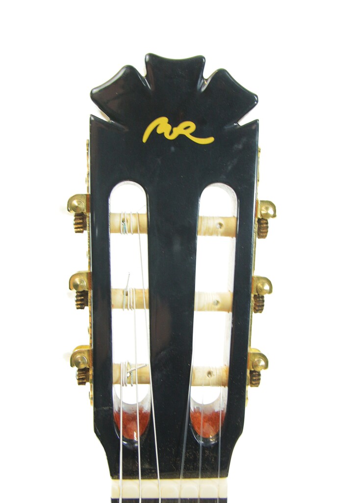 Nahaufnahme Der Kopfplatte Der Manuel Rodriguez Jr Klassische Gitarre Mit Goldenen Stimmwirbeln, Schwarzem Finish Und Einem Gelben Logo Im Signaturstil Oben Auf Weißem Hintergrund.