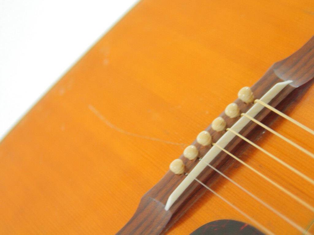 Close-Up Of The Guild D-44 1967 Acoustic Guitar’s Body, Highlighting Its Wooden Bridge, Six Strings, And White Bridge Pins On A Light Brown Finish. Background Is Softly Blurred.