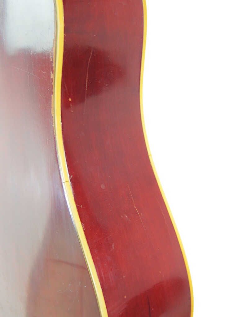 Close-Up Of The Side Of A Red-Brown Guild D-44 1967 Acoustic Guitar With Yellow Trim, Highlighting Its Glossy Wooden Finish And Subtle Reflections Against A White Background.