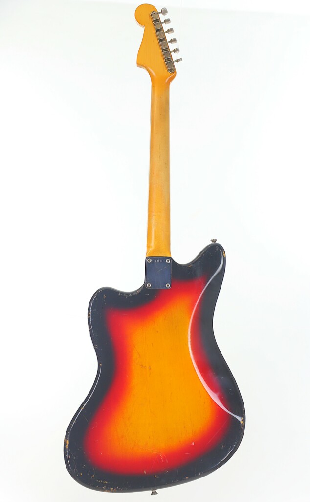 A Fender Jazzmaster 1963 Electric Guitar, Shown From The Back Against A White Background, Displays Its Sunburst Finish In Red, Orange, And Black With A Wooden Neck And Metal Tuners.