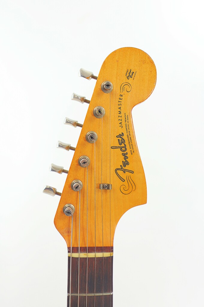 Close-Up Of The Fender Jazzmaster 1963 Electric Guitar Headstock Showing Six Tuning Pegs And Strings, Set Against A White Background.