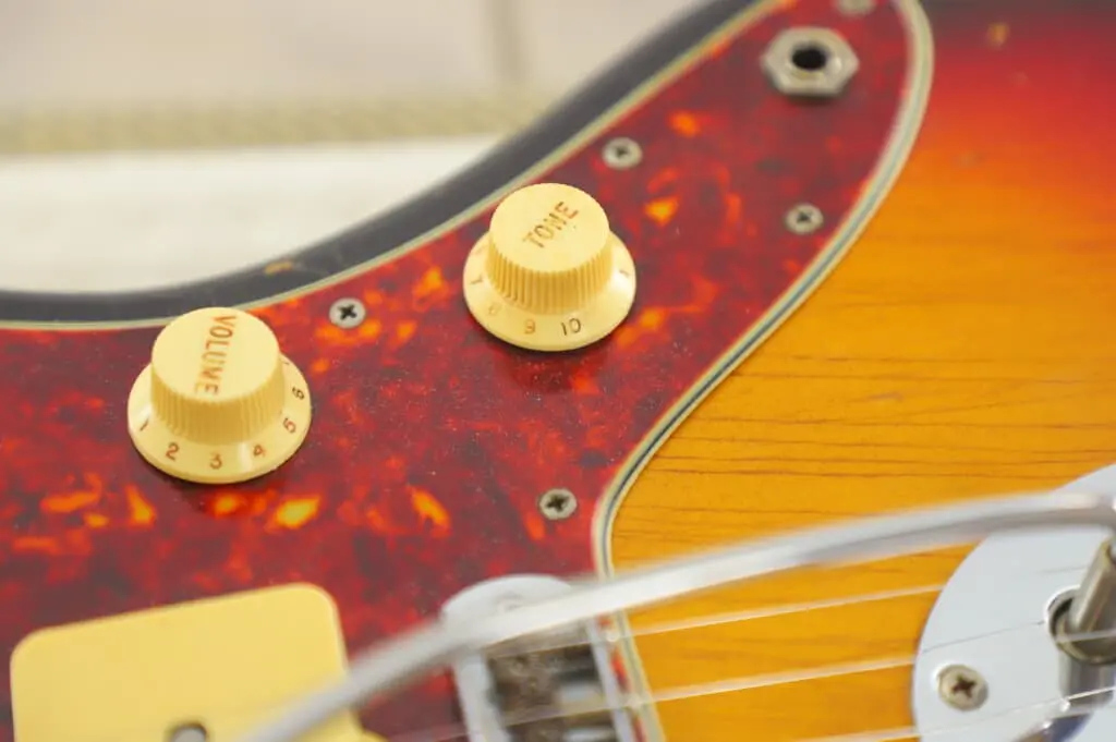 Close-Up Of A Fender Jazzmaster 1963 Electric Guitar’s Body, Featuring The Volume And Tone Knobs On A Reddish-Brown Pickguard With Visible Strings And Wood Grain Detail.