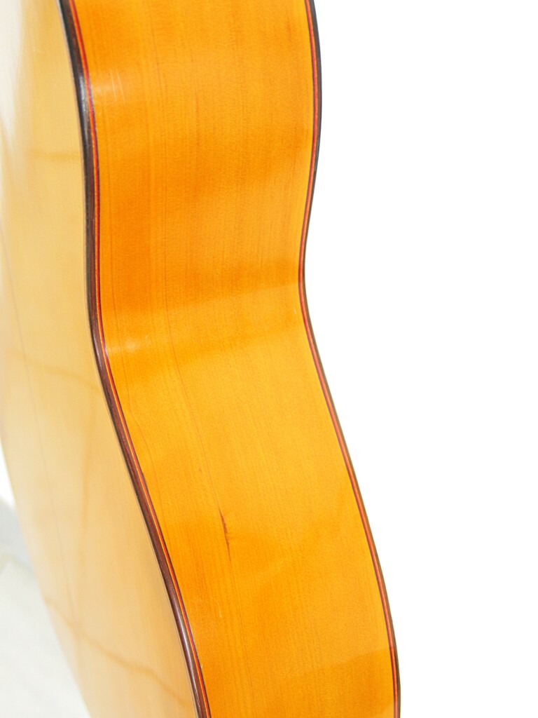 Close-Up Of The Side Of A Hermanos Conde 1966 Faustino Conde Flamenco Guitar, Highlighting Its Light Wood Grain And Smooth, Curved Surface Set Against A White Background.