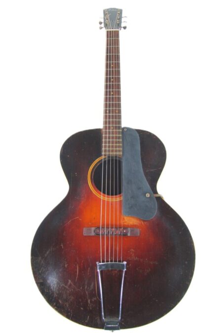 A Gibson L-4 1932 Acoustic Guitar with a sunburst finish, dark brown body, lighter center, black pickguard, and edge wear is pictured on a white background.