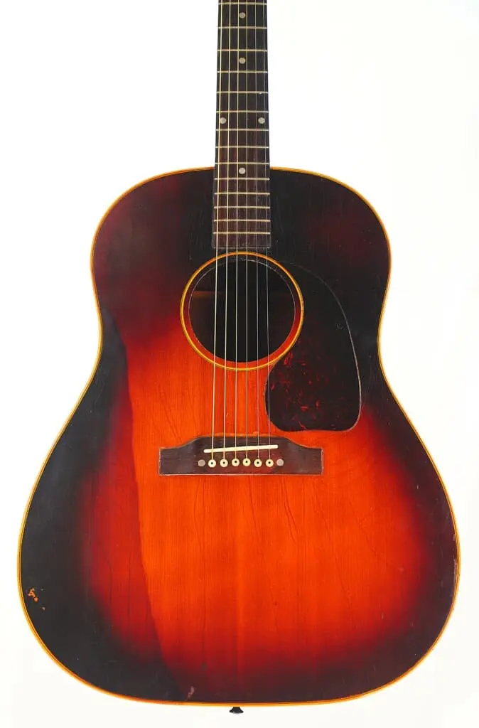 A Gibson J-45 1955 Acoustic Guitar With A Sunburst Finish, Featuring Six Strings And A Black Pickguard, Is Displayed Against A Plain White Background.