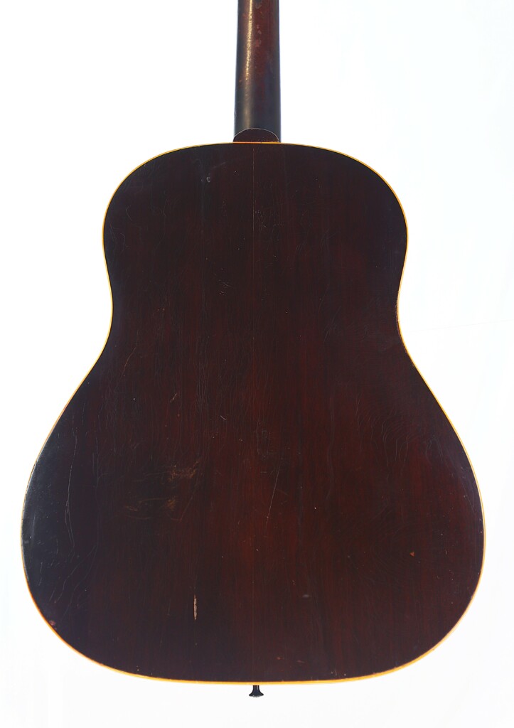The Image Shows The Back Of A Gibson J-45 1955 Acoustic Guitar, Featuring A Dark Wood Finish With A Glossy Surface, Visible Wood Grain, Some Light Scratches, And The Neck Extending From The Top Center.
