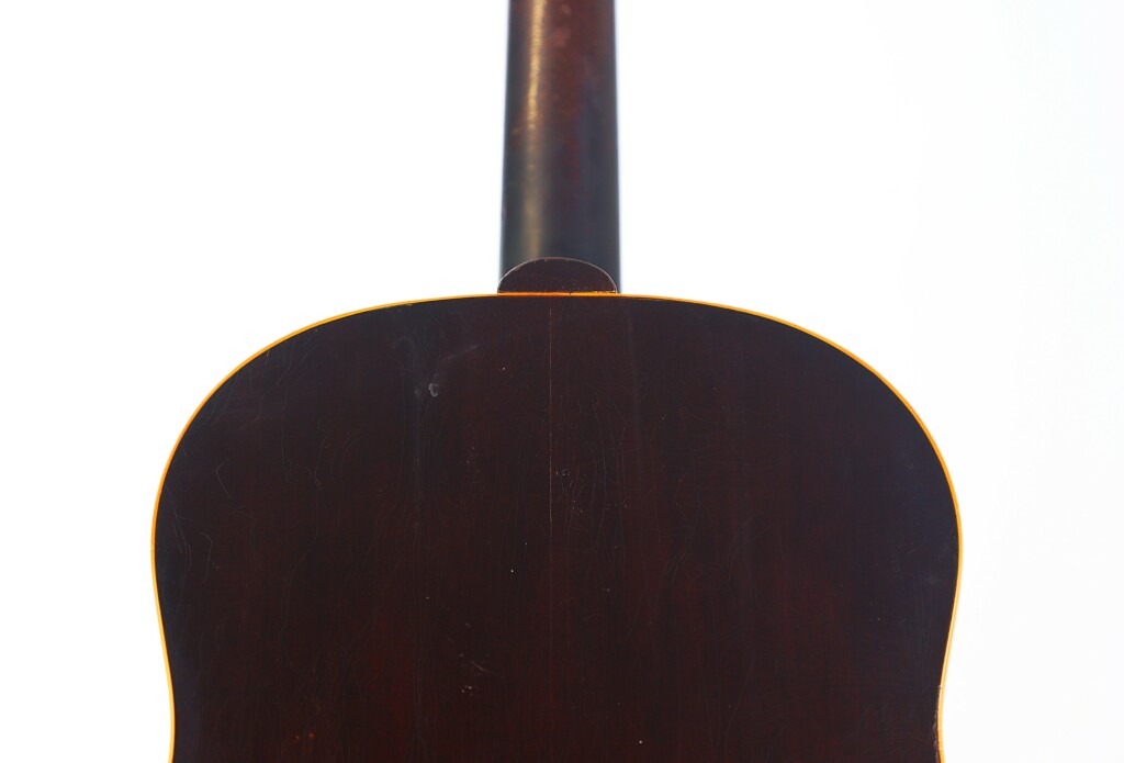 Close-Up Of The Back Of The Gibson J-45 1955 Acoustic Guitar, Highlighting Its Dark Wood Body And Neck On A Plain White Background. The Top Edge Of The Body And Lower Neck Are Clearly Visible.