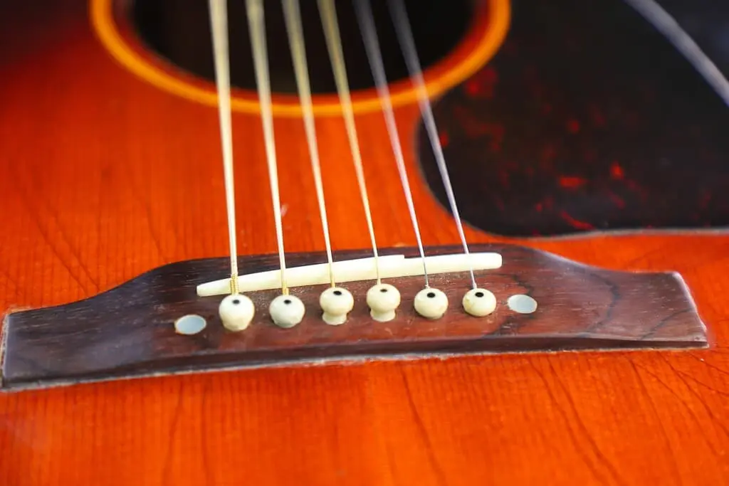 Close-Up Of The Gibson J-45 1955 Acoustic Guitar’s Bridge, Featuring Six Strings With White Bridge Pins On Its Wooden Body, Showcasing The Wood Grain And Warm Tone.