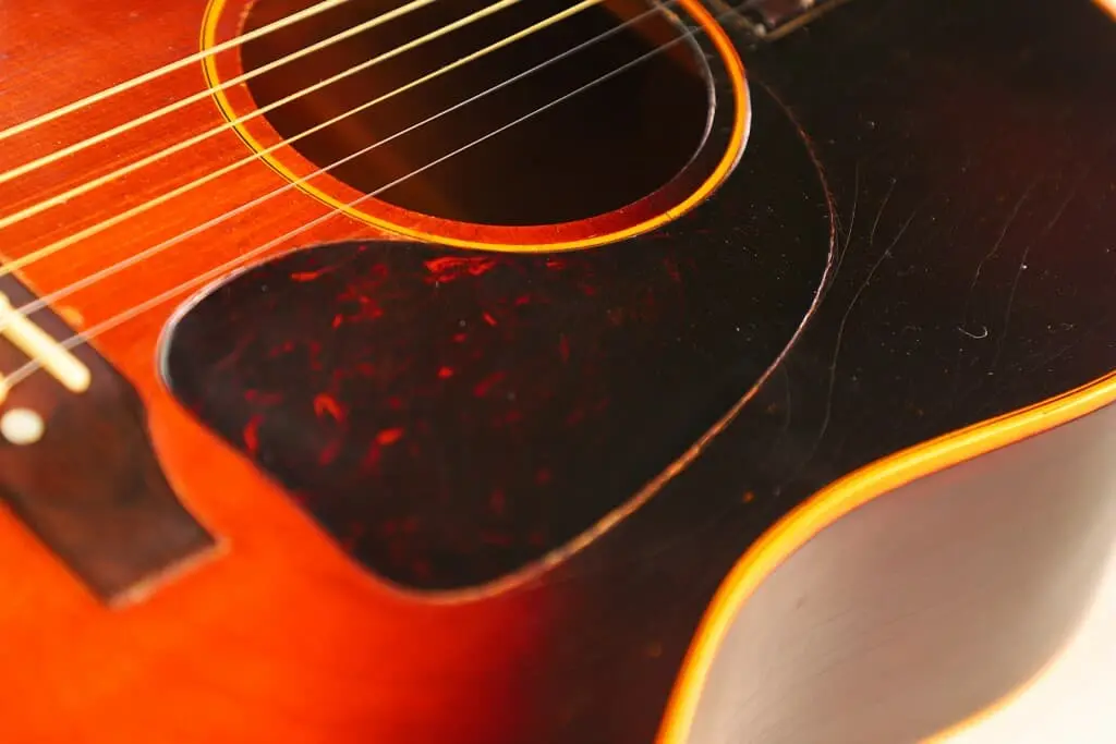Close-Up Of The Gibson J-45 1955 Acoustic Guitar Body, Highlighting Its Strings, Sound Hole, Pickguard, And Warm Brown Wood Finish With Visible Grain And Subtle Scratches.