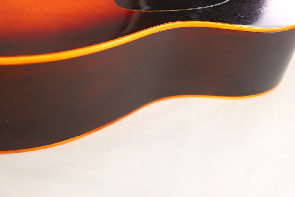 Close-Up Of The Side Of A Gibson J-45 1955 Acoustic Guitar, Featuring A Dark Brown Finish With Orange Edging, Set Against A White Background.