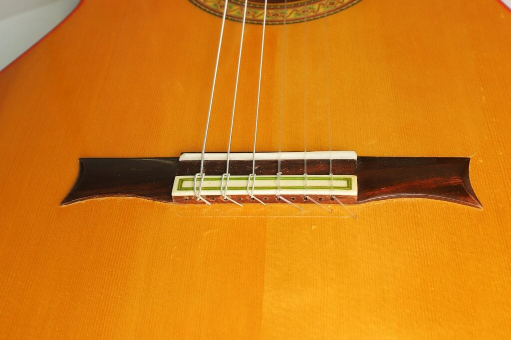 Nahaufnahme des Stegs und der Saiten einer hölzernen Flamenco-Gitarre von Gerardo Escobedo aus dem Jahr 2018. Nahaufnahme des Stegs und der Saiten einer hölzernen Flamenco-Gitarre von Gerardo Escobedo aus dem Jahr 2018.