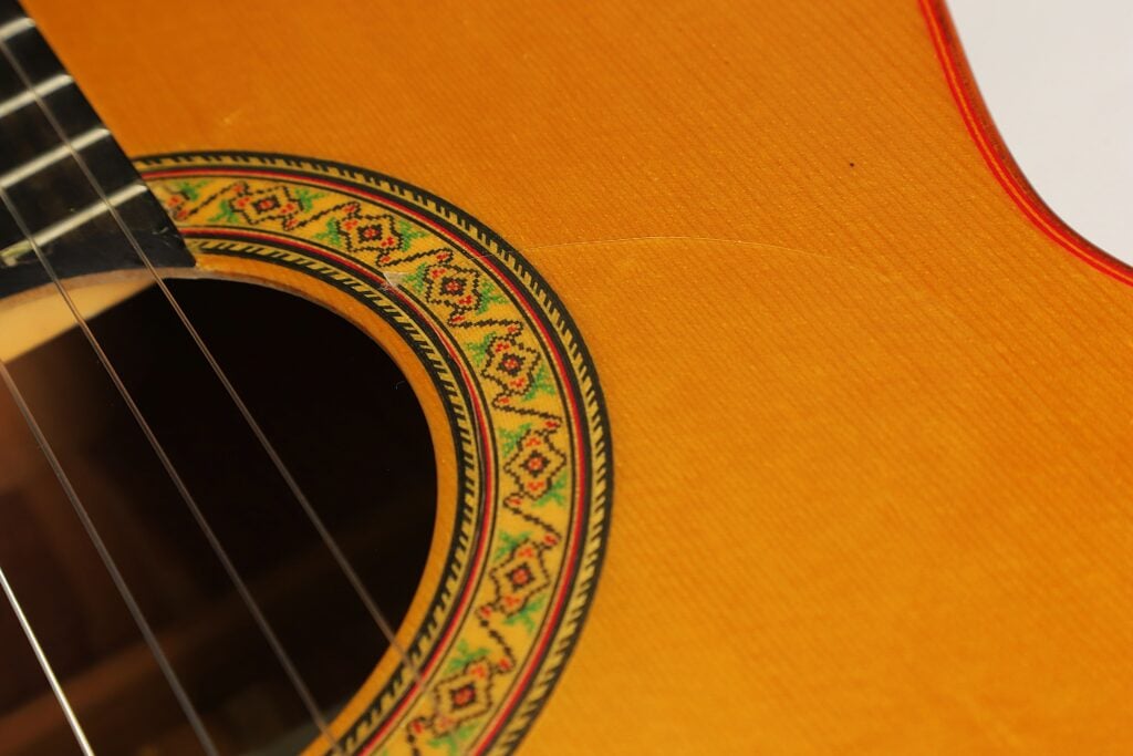 Nahaufnahme des Schalllochs einer Flamenco-Gitarre von Gerardo Escobedo aus dem Jahr 2018 mit einer farbenfrohen Zierrosette und einem sichtbaren Riss im Holz der Decke. Nahaufnahme des Schalllochs einer Flamenco-Gitarre von Gerardo Escobedo aus dem Jahr 2018 mit einer farbenfrohen Zierrosette und einem sichtbaren Riss im Holz der Decke.