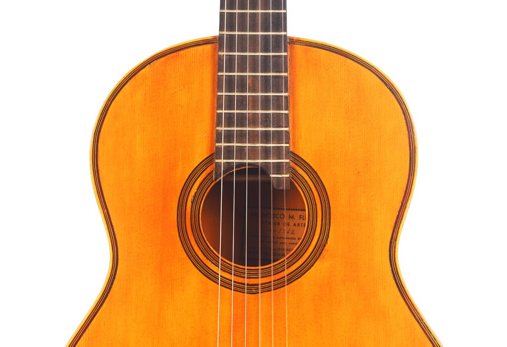 Nahaufnahme von Korpus und Hals der klassischen Akustikgitarre Francisco Manuel Fleta 1962. Hervorzuheben sind die Holzoberfläche, die Saiten und ein Teil des Schalllochs vor einem weißen Hintergrund. Nahaufnahme von Korpus und Hals der klassischen Akustikgitarre Francisco Manuel Fleta 1962. Hervorzuheben sind die Holzoberfläche, die Saiten und ein Teil des Schalllochs vor einem weißen Hintergrund.