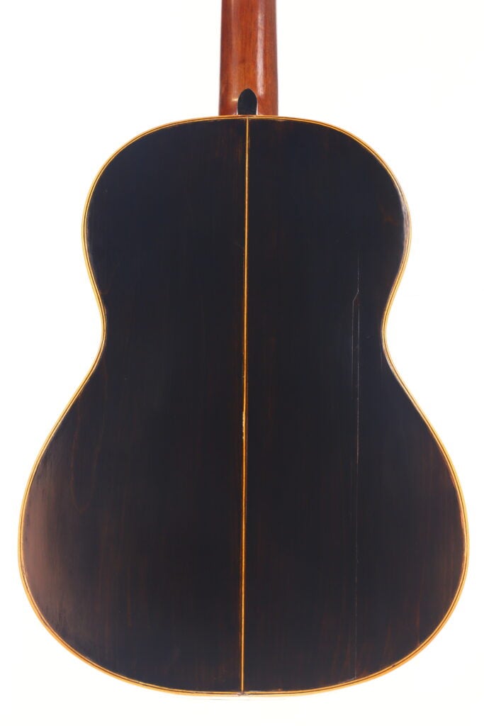 Die Rückseite der Akustikgitarre Francisco Manuel Fleta 1962 hat eine dunkle Holzoberfläche, eine sichtbare Mittelnaht und eine helle Zierleiste an den Rändern. Der elegante Hals des Instruments erstreckt sich von der Oberseite des Bildes. Die Rückseite der Akustikgitarre Francisco Manuel Fleta 1962 hat eine dunkle Holzoberfläche, eine sichtbare Mittelnaht und eine helle Zierleiste an den Rändern. Der elegante Hals des Instruments erstreckt sich von der Oberseite des Bildes.