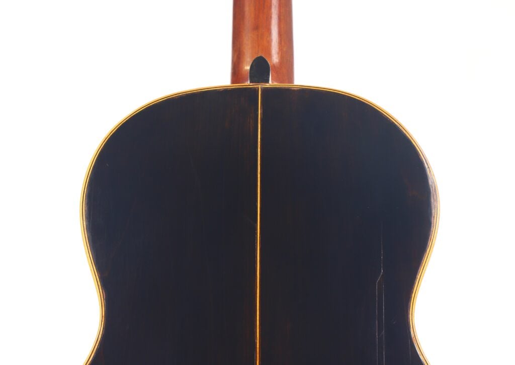 Nahaufnahme des Bodens einer Akustikgitarre von Francisco Manuel Fleta aus dem Jahr 1962 in Dunkelbraun mit heller Zierleiste und einer sichtbaren Mittelnaht, dargestellt vor einem weißen Hintergrund. Nahaufnahme des Bodens einer Akustikgitarre von Francisco Manuel Fleta aus dem Jahr 1962 in Dunkelbraun mit heller Zierleiste und einer sichtbaren Mittelnaht, dargestellt vor einem weißen Hintergrund.