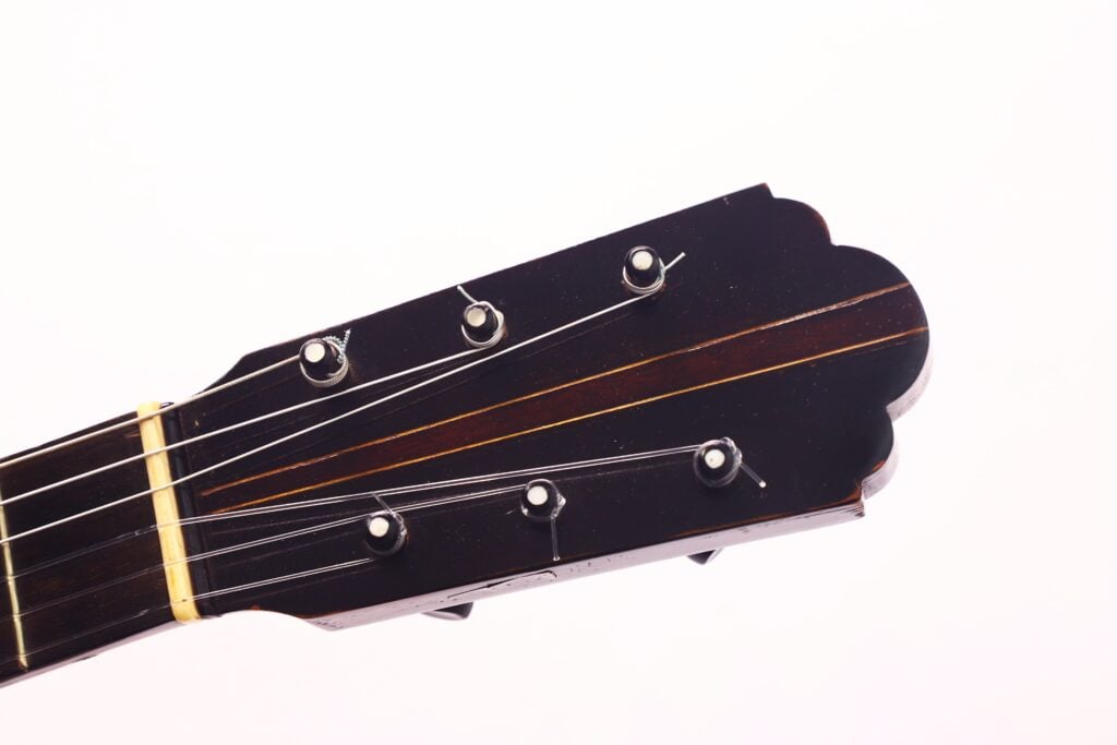 Nahaufnahme der Kopfplatte einer Gitarre von Francisco Manuel Fleta aus dem Jahr 1962 mit sechs Wirbeln und Saiten, fotografiert vor einem schlichten weißen Hintergrund. Nahaufnahme der Kopfplatte einer Gitarre von Francisco Manuel Fleta aus dem Jahr 1962 mit sechs Wirbeln und Saiten, fotografiert vor einem schlichten weißen Hintergrund.