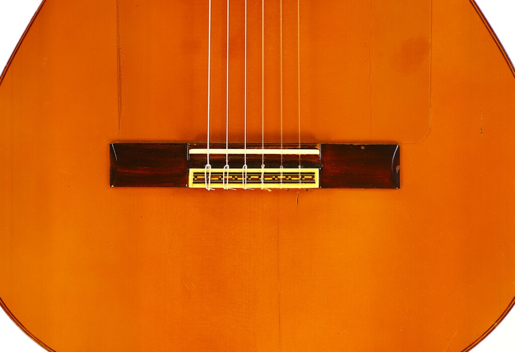 Close-Up Of A Manuel G. Mayoral 1980 Flamenco Guitar, Showing The Bridge, Strings, And Detailed Wood Grain On Its Warm Orange-Brown Body That Highlights Its Expert Craftsmanship.