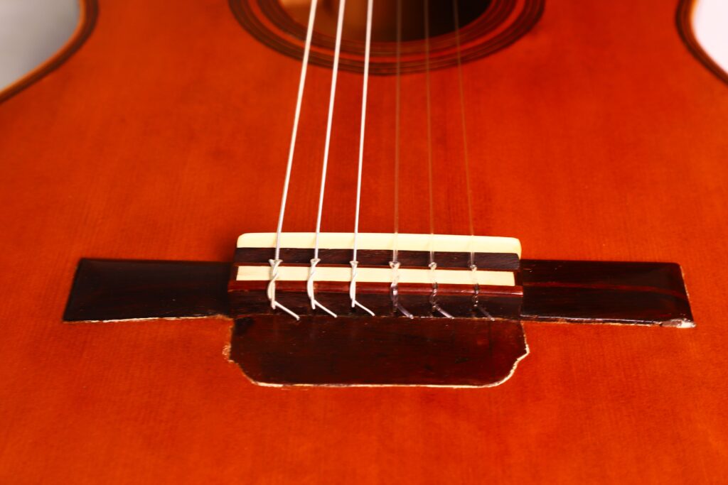 Nahaufnahme des Stegs und der Saiten einer klassischen Gitarre von Francisco Manuel Fleta aus dem Jahr 1962, wobei die Holzmaserung und die komplizierten Details hervorgehoben werden. Nahaufnahme des Stegs und der Saiten einer klassischen Gitarre von Francisco Manuel Fleta aus dem Jahr 1962, wobei die Holzmaserung und die komplizierten Details hervorgehoben werden.