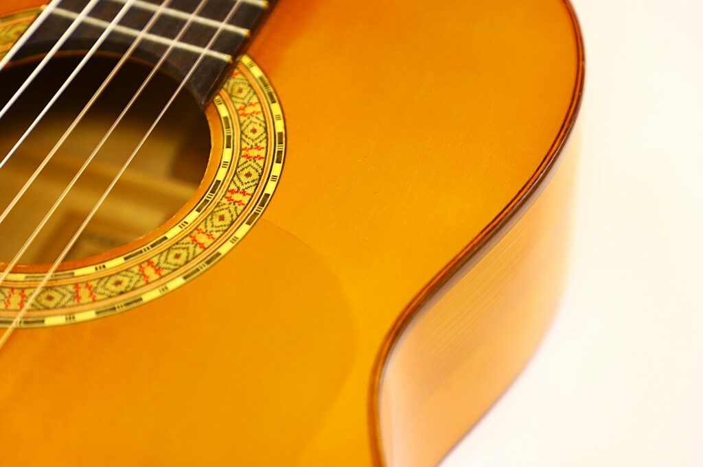 Close-Up Of A Manuel G. Mayoral 1980 Flamenco Guitar, Highlighting Its Strings, Rosette-Decorated Sound Hole, And Glossy Wooden Body Against A Light Background.