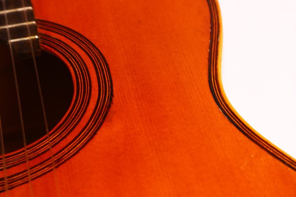 Nahaufnahme des Korpus der Akustikgitarre Francisco Manuel Fleta 1962. Hervorzuheben sind das Schallloch, die Saiten und die filigranen Kreismuster auf der warmen braunen Holzoberfläche. Nahaufnahme des Korpus der Akustikgitarre Francisco Manuel Fleta 1962. Hervorzuheben sind das Schallloch, die Saiten und die filigranen Kreismuster auf der warmen braunen Holzoberfläche.