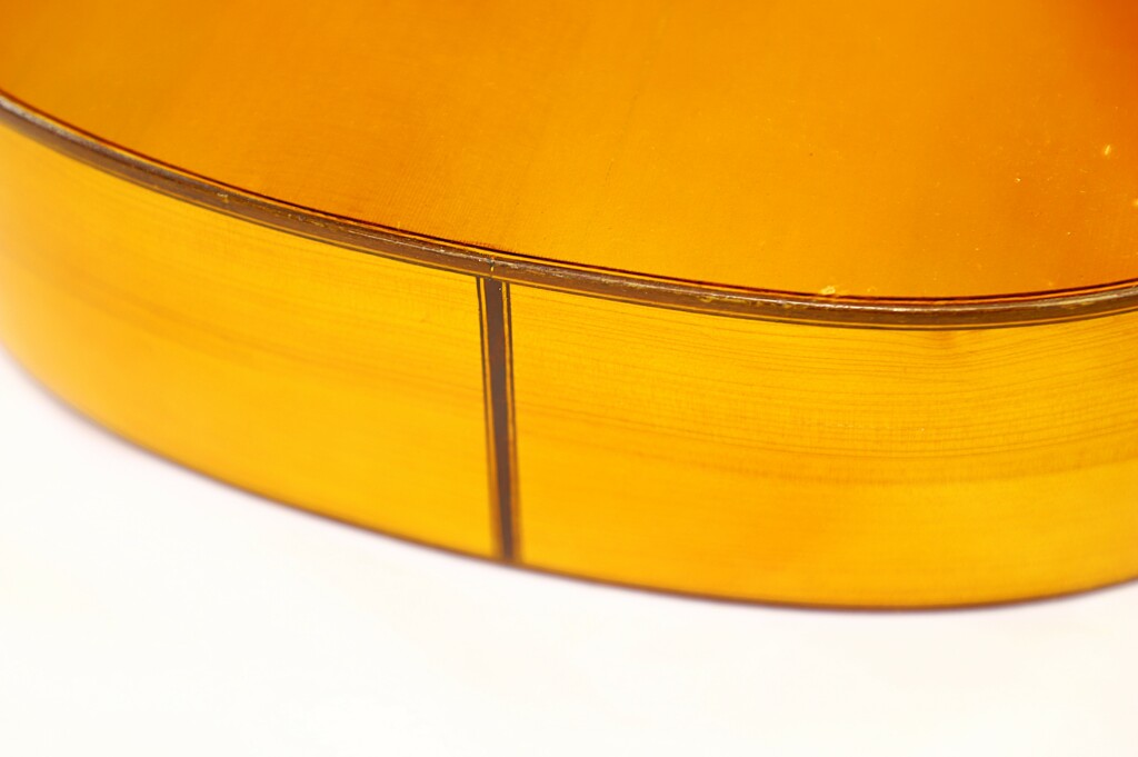 Close-Up Of The Side And Back Edge Of A Manuel G. Mayoral 1980 Flamenco Guitar, Showing Detailed Wood Grain, Glossy Yellow Finish, And A Visible Seam.