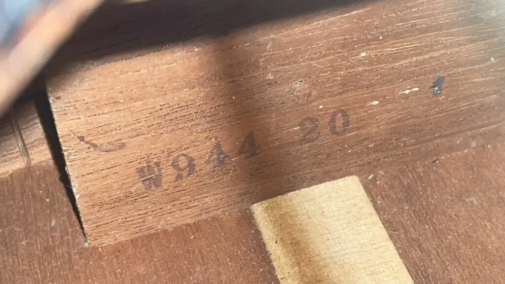 Close-Up Of A Gibson J-45 1955 Acoustic Guitar’s Light Brown Wood Surface Shows Visible Grain, A Small Lighter Patch Near The Bottom, And #944 90 Stamped In Black Ink.