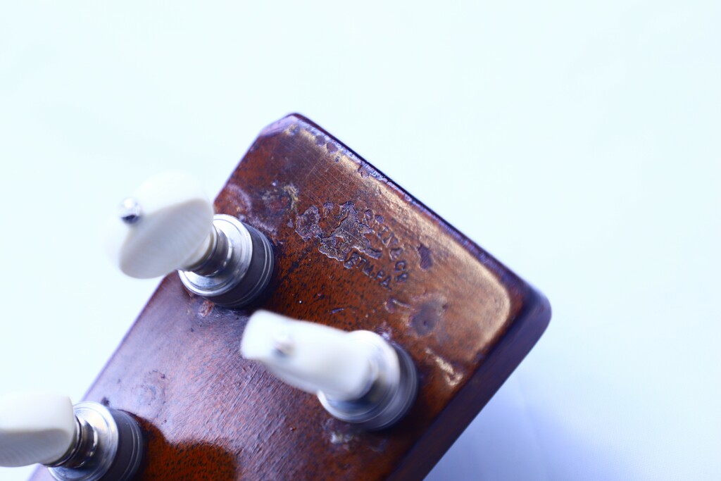Close-Up Of The Martin Om-28 1931 Acoustic Guitar Headstock Shows Three White Tuning Pegs And Visible Wear, Such As Scratches And Faded Lettering, Against A Light Background.