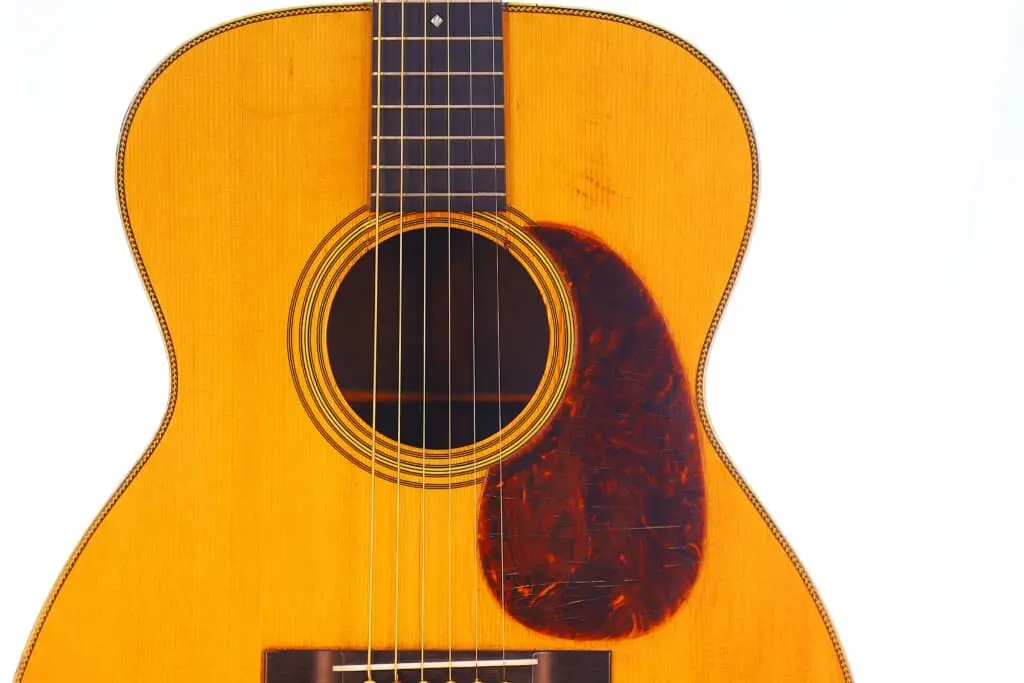 Close-Up Of The Martin Om-28 1931 Acoustic Guitar Body, Highlighting Its Strings, Soundhole, Dark Brown Pickguard, And Light Wood Finish.