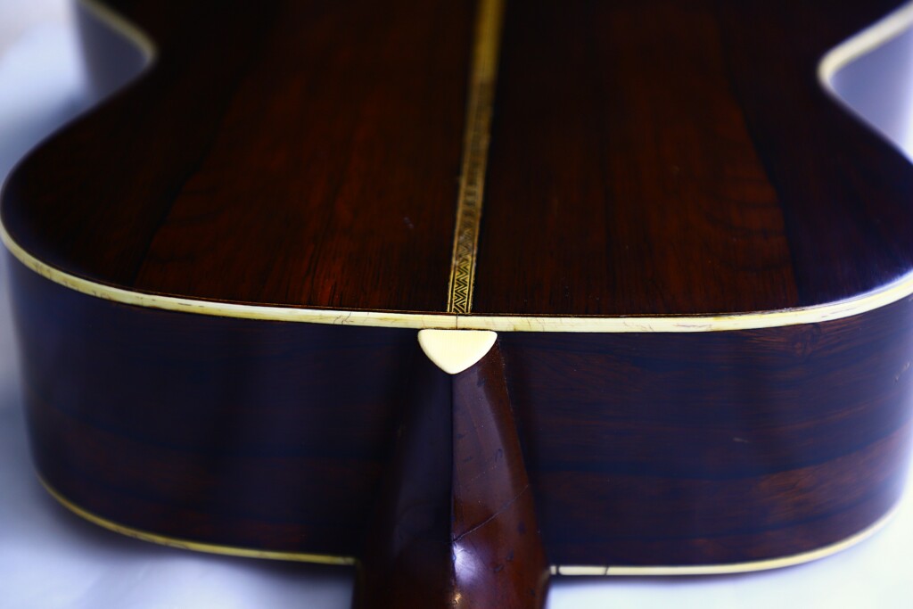 Close-Up Of The Back Of The Martin Om-28 1931 Acoustic Guitar, Featuring Dark Wood Grain, Cream Edge Binding, A Decorative Center Inlay Strip, And A Partially Visible Neck Heel.