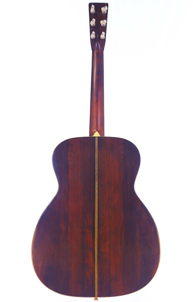 The Martin Om-28 1931 Acoustic Guitar Is Shown From The Back, Highlighting Its Dark Wooden Body With A Visible Center Seam, Smooth Polished Finish, And Visible Headstock With Tuning Pegs.