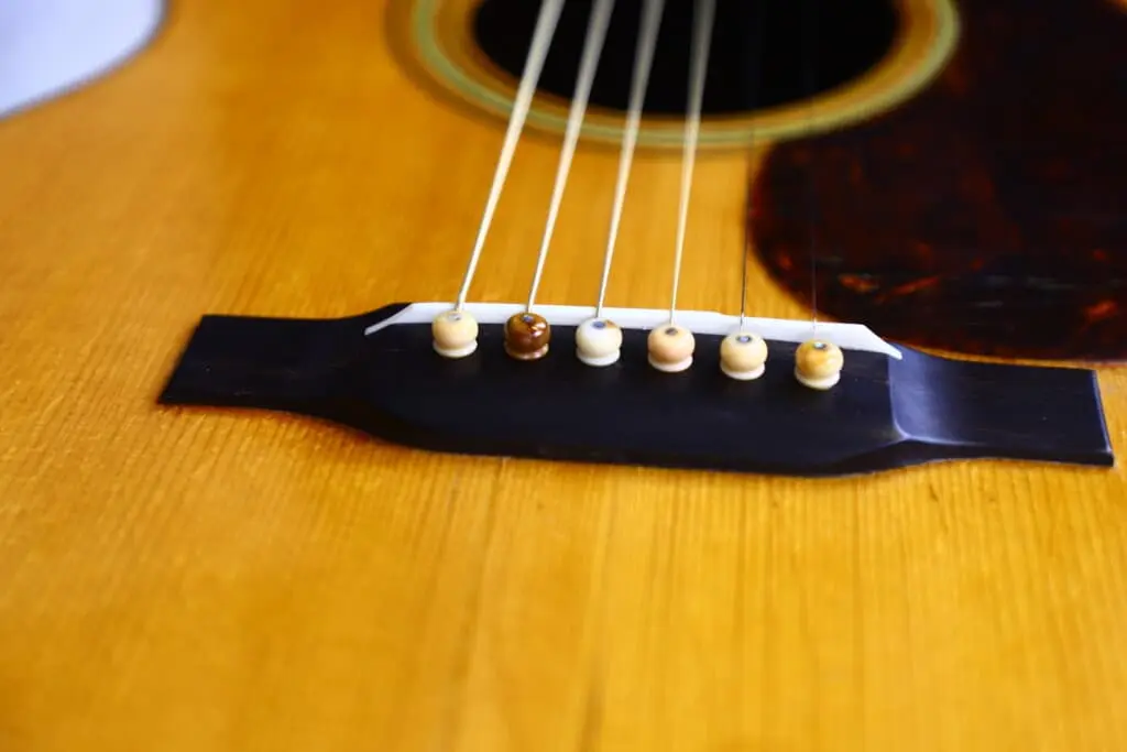Close-Up Of The Martin Om-28 1931 Acoustic Guitar Bridge, Featuring Six Strings Secured By Bridge Pins On Its Wooden Body.