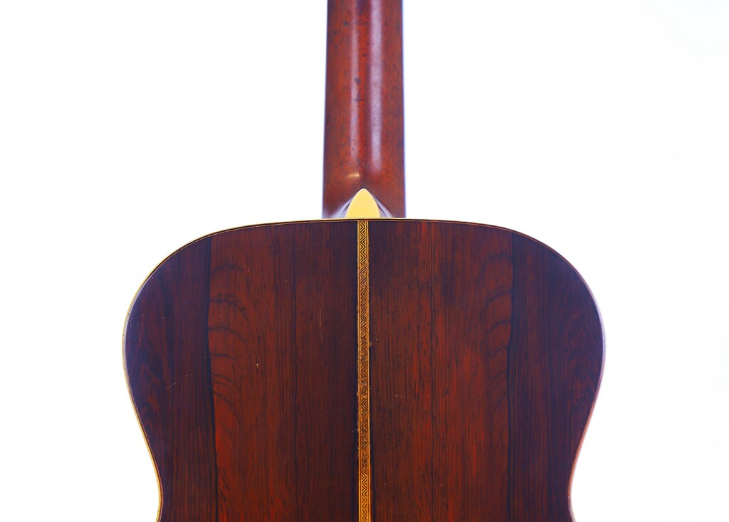 Close-Up Of The Martin Om-28 1931 Acoustic Guitar’s Back, Highlighting Its Rich Dark Wood Grain, A Central Decorative Inlay Strip, And The Upward-Extending Neck.