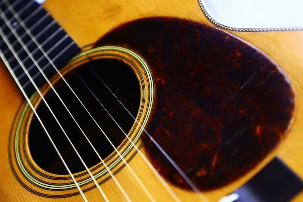 Close-Up Of The Martin Om-28 1931 Acoustic Guitar, Featuring Its Soundhole, Strings, And Distinct Dark Tortoiseshell-Patterned Pickguard On The Wooden Body.