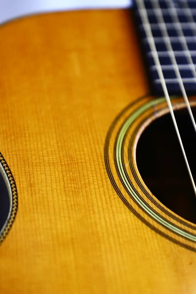 Close-Up Of The Martin Om-28 1931 Acoustic Guitar Highlighting Its Strings, Partial Sound Hole, And Wooden Body Featuring A Detailed Rosette Pattern Around The Opening.