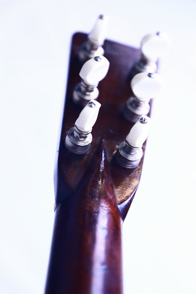 Close-Up Of The Martin Om-28 1931 Acoustic Guitar Headstock’s Back, Featuring Six White Tuning Pegs On A Wooden Neck Against A Bright, Blurred Background.