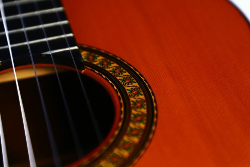 Nahaufnahme einer José Ramírez 1a 1987 Klassischen Gitarre, die ihre Saiten, den Griffbrettbereich und die verzierte Rosette um das Schallloch auf dem polierten Holzkorpus hervorhebt.