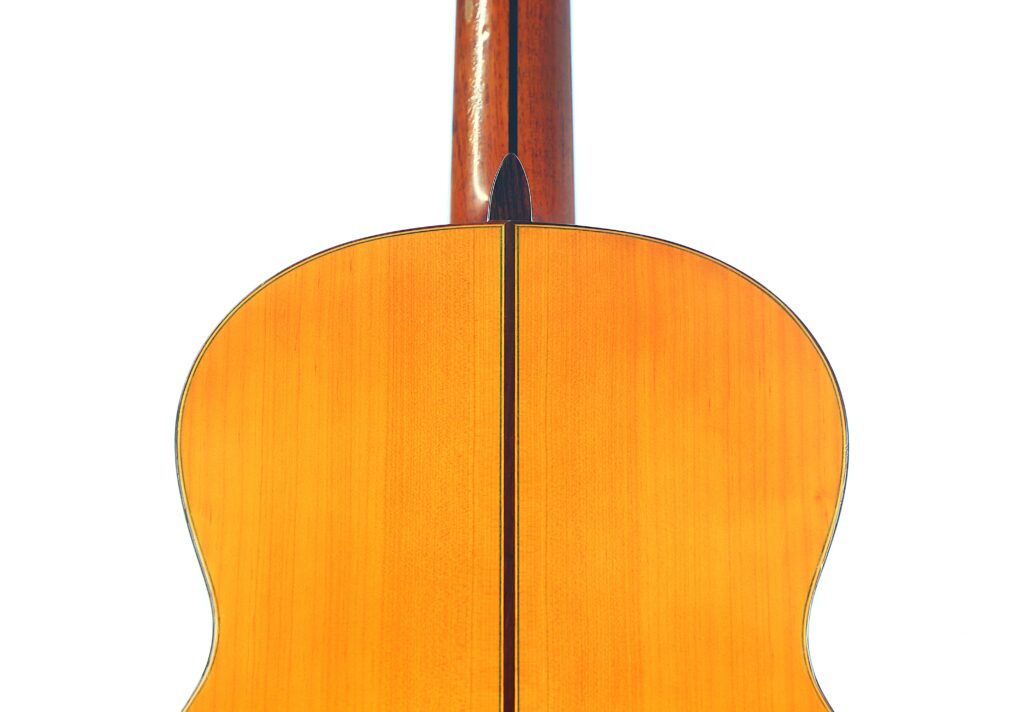 The Image Shows The Back Of A Lorenzo Alvarez 1982 Flamenco Guitar, Featuring Light Wood With A Dark Central Stripe, And The Neck Visible At The Top, Set Against A Plain White Background.